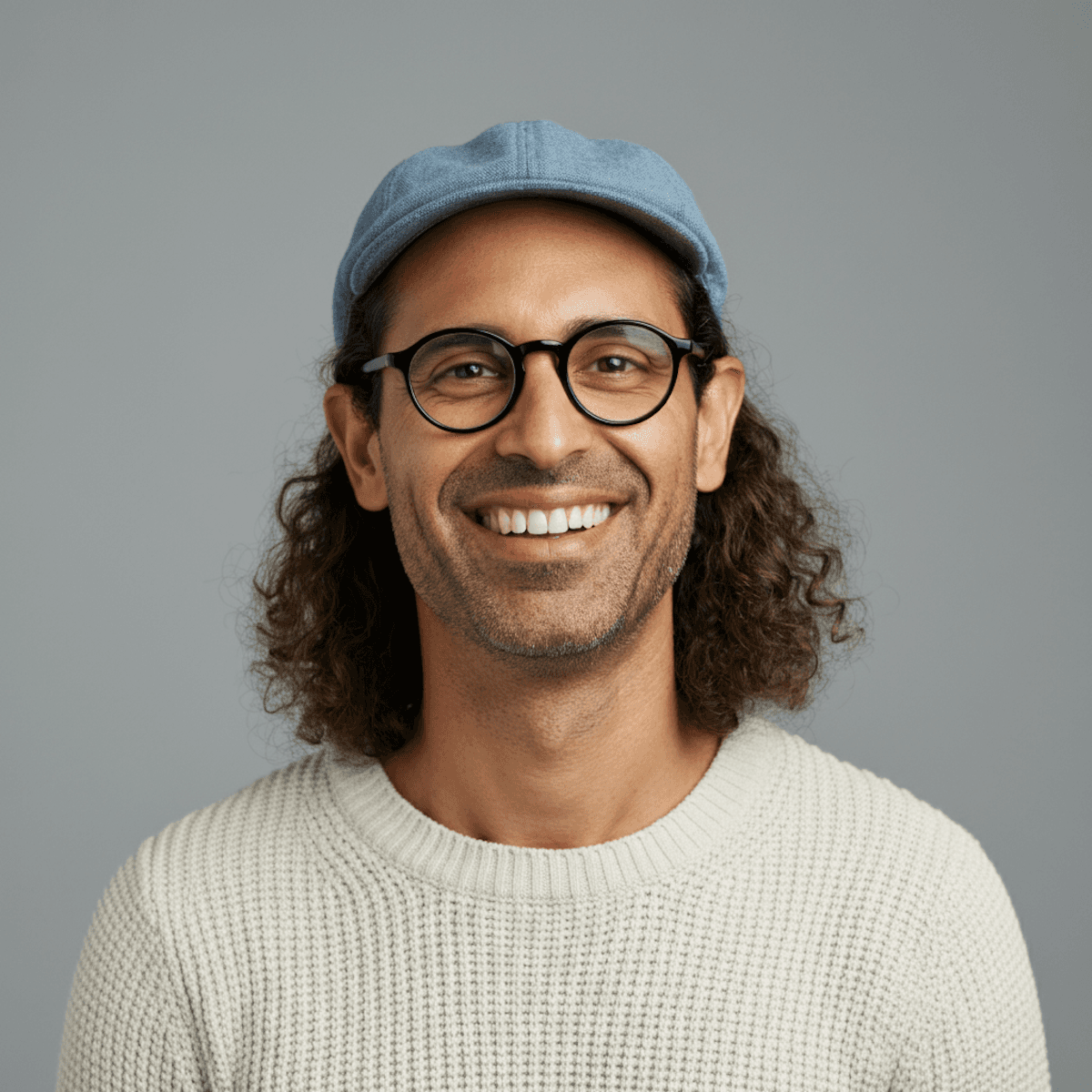 A stylish individual in a cream knit beanie and cardigan, paired with a dark gray shirt, set against a neutral gray background.